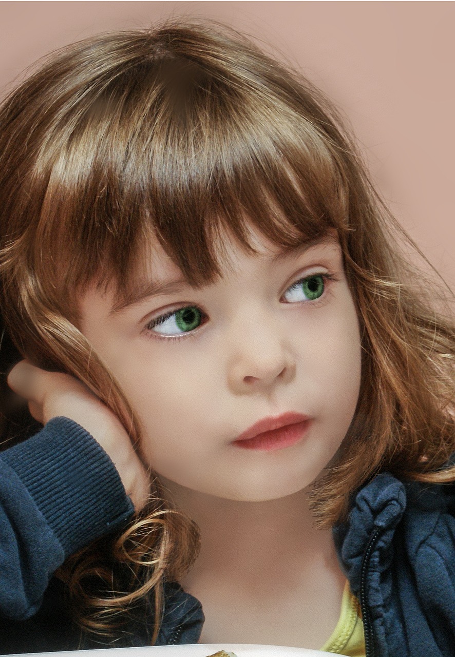 Un jeune enfant aux cheveux châtain clair et aux yeux verts pose sa tête sur sa main, regardant sur le côté avec une expression rêveuse. Ils portent un haut bleu foncé, peut-être perdus dans leurs pensées à cause des Troubles du Déficit de l'Attention.