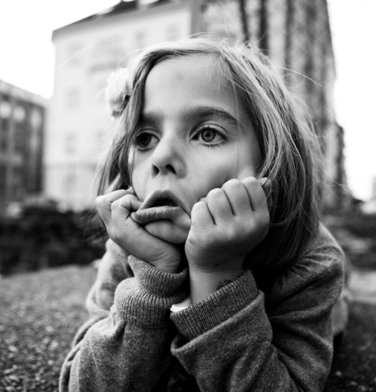 Un jeune enfant pose son menton sur ses mains, le regard pensif au loin, peut-être victime de problèmes du sommeil chez l’enfant lié à l’hyperactivité.