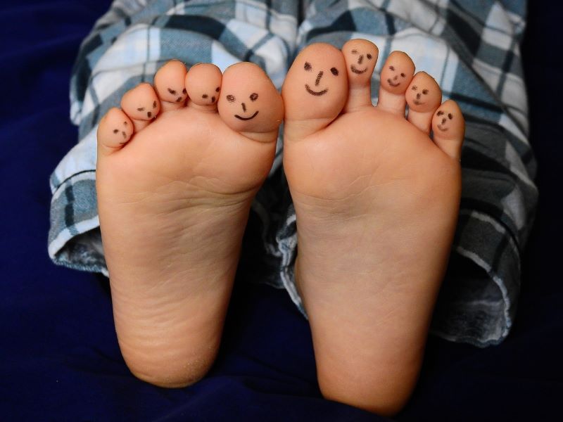 Des pieds aux visages souriants dessinés sur les orteils, vêtus d'un bas de pyjama à carreaux, évoquent un clin d'œil ludique à la réflexologie plantaire alors qu'ils reposent sur un fond bleu foncé.